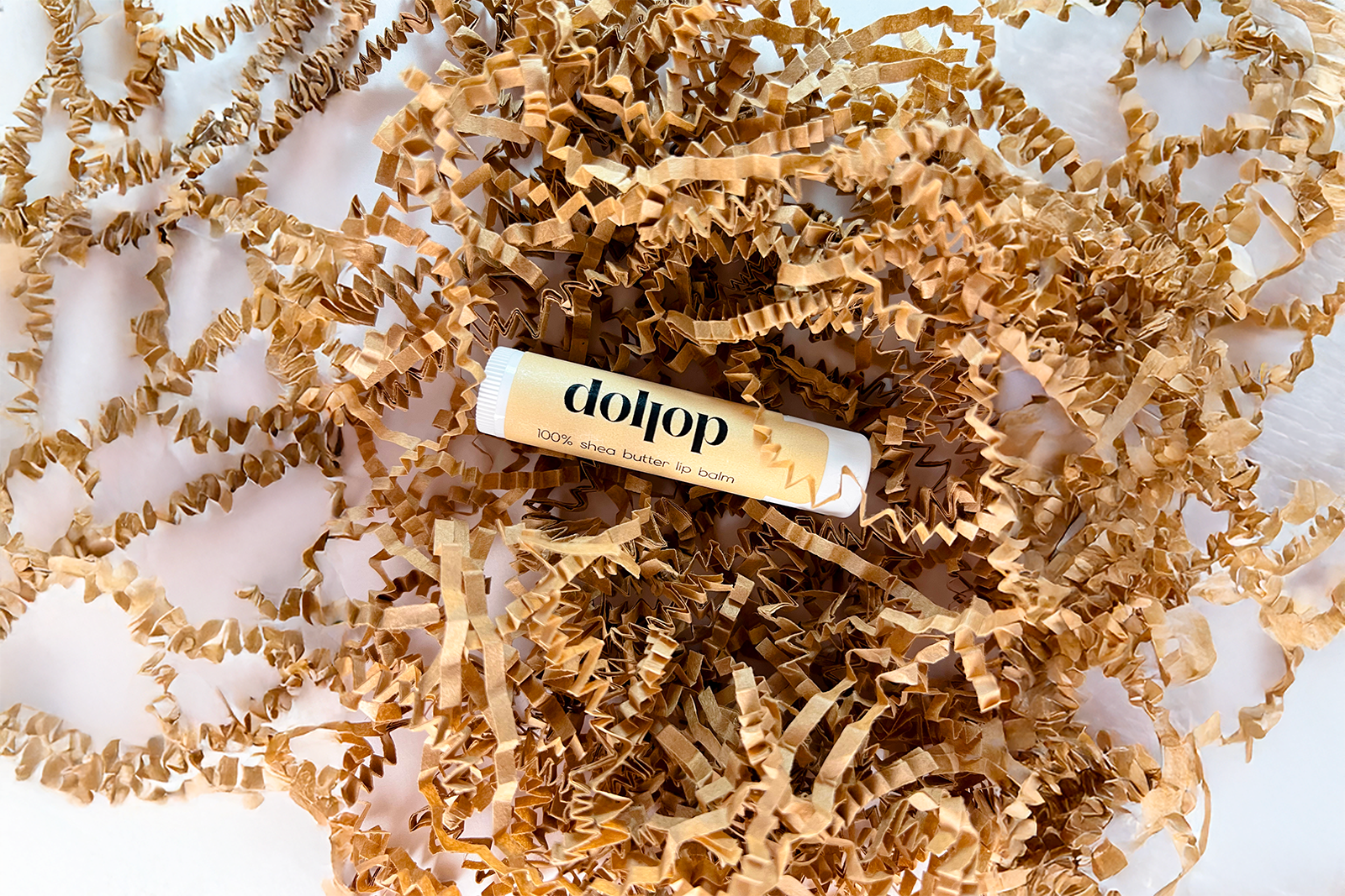 single tube of lip balm on crumpled kraft paper with 'dollop' branding.